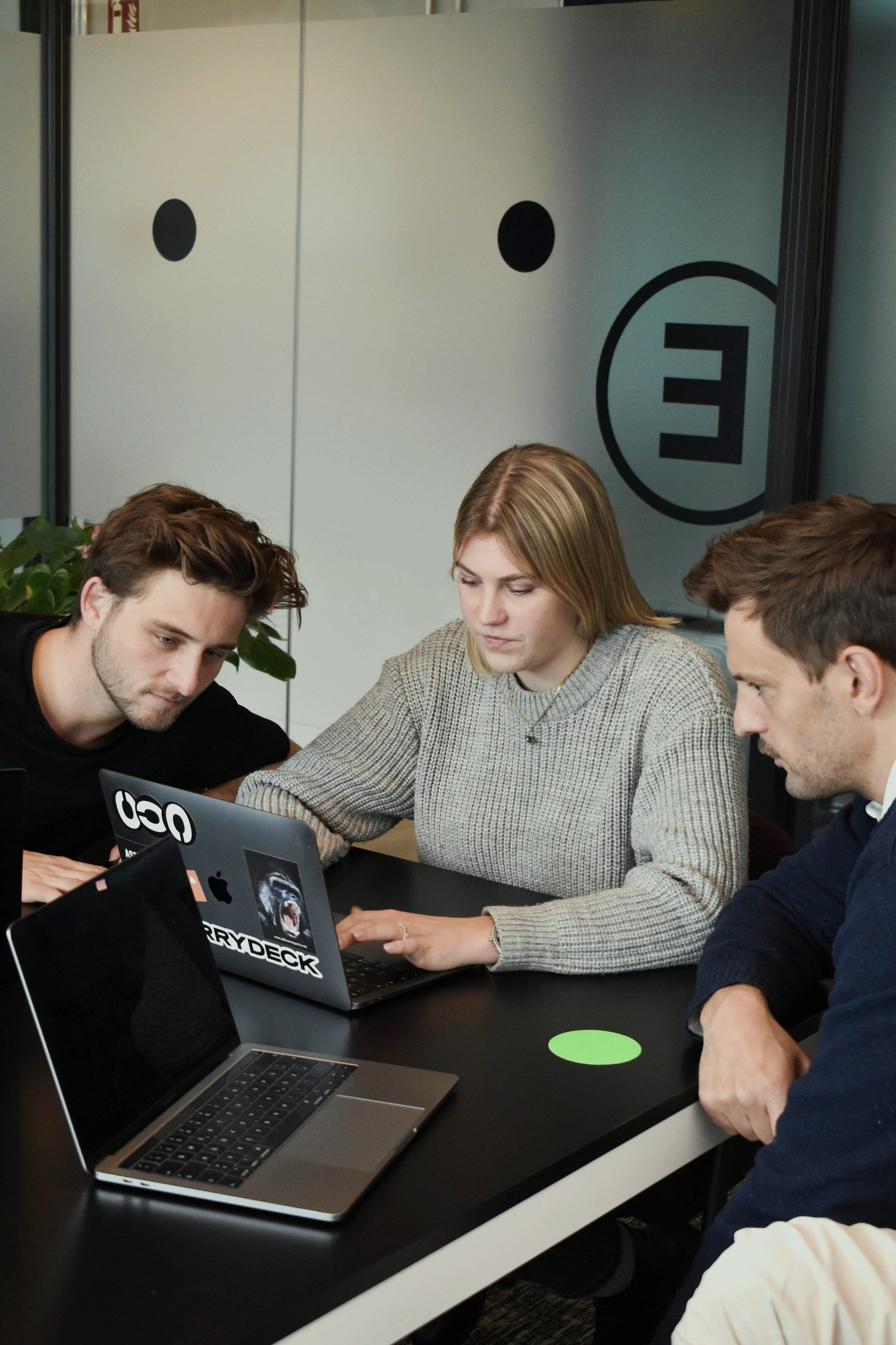 Three people working on a laptop at a table in a small office